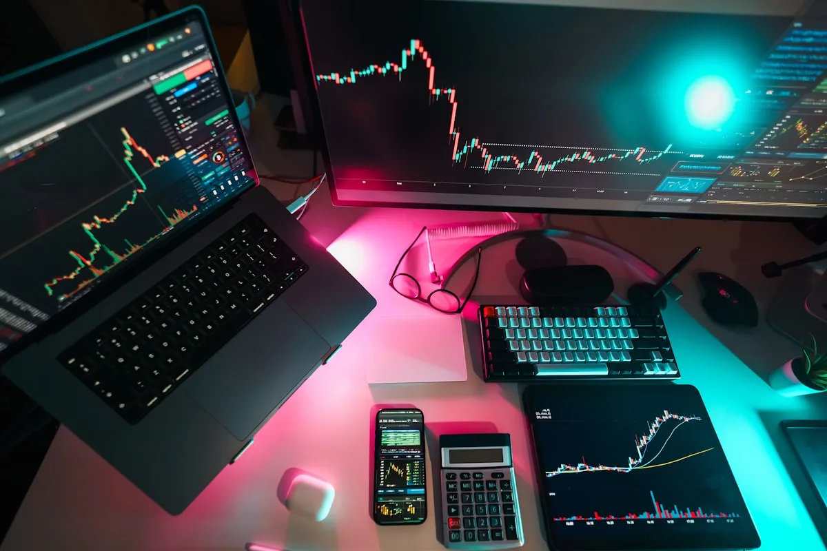 Setup de três telas usado em trading e análise de gráficos Setup de trading com notebook, monitor curvo e tablet em mesa com iluminação rosa e ciano