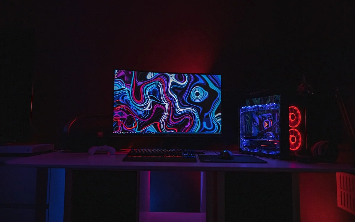 Mesa gamer com LED RGB — iluminação ambiente e bias lighting Mesa gamer com fita de LED RGB embaixo do tampo criando halo de luz ambiente no setup