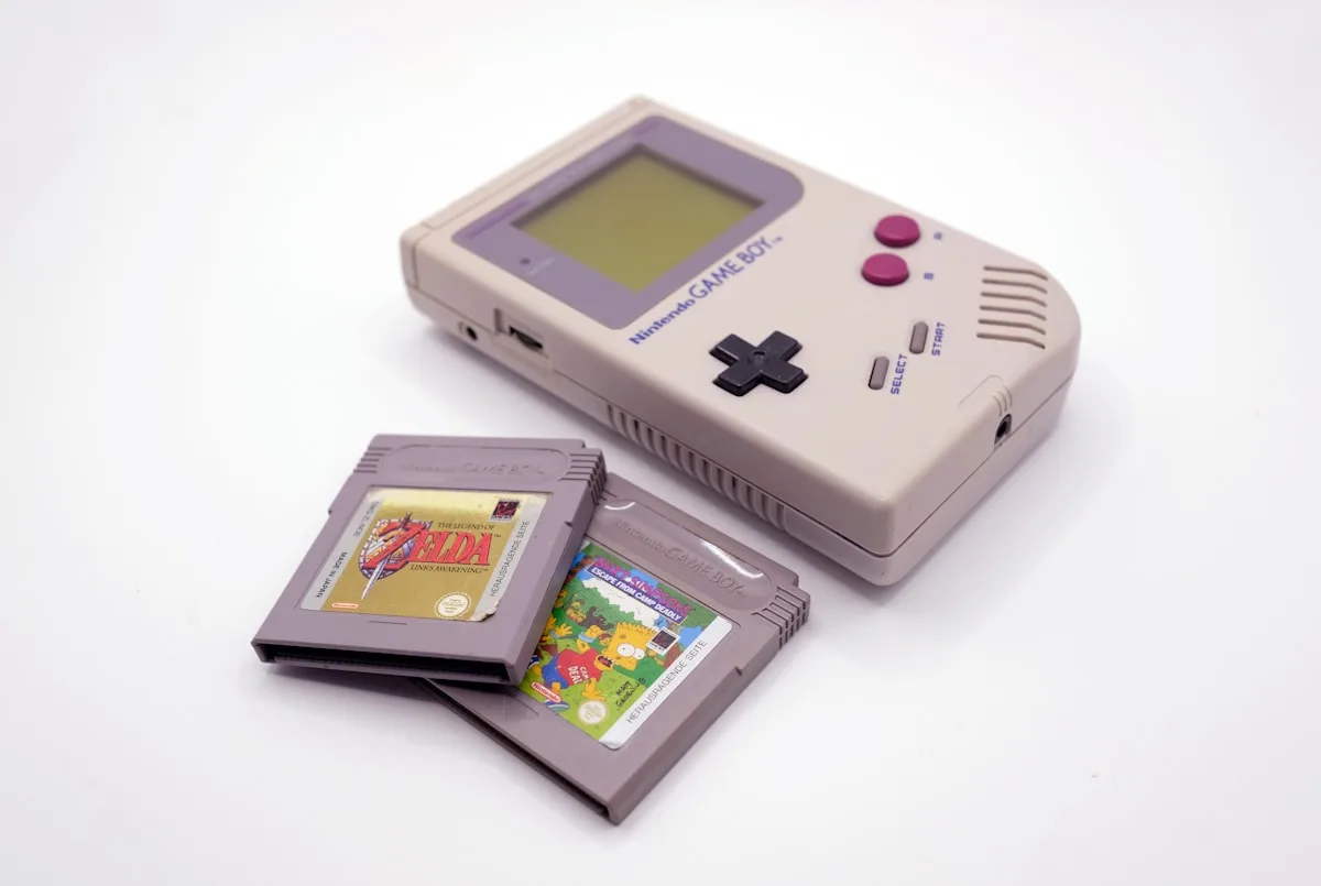 Game Boy original cinza ao lado de dois cartuchos de jogo sobre superfície branca