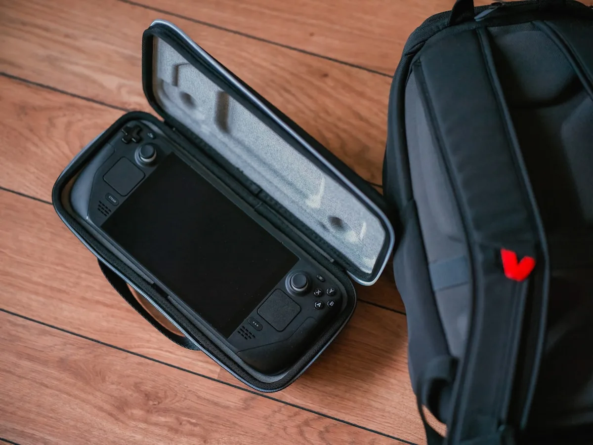 Console portátil guardado em estojo acolchoado ao lado de mochila gamer preta com detalhe vermelho