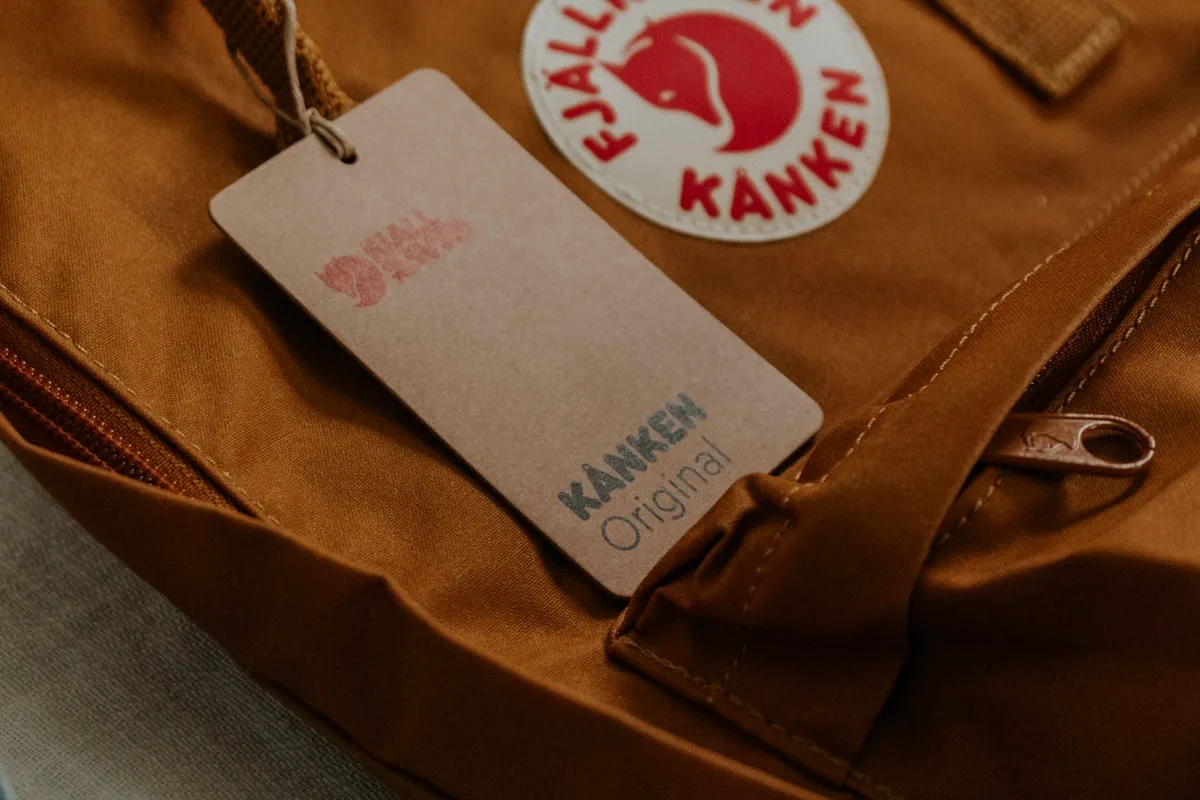 Etiqueta de marca presa a uma mochila colorida, com logotipo em destaque perto do zíper