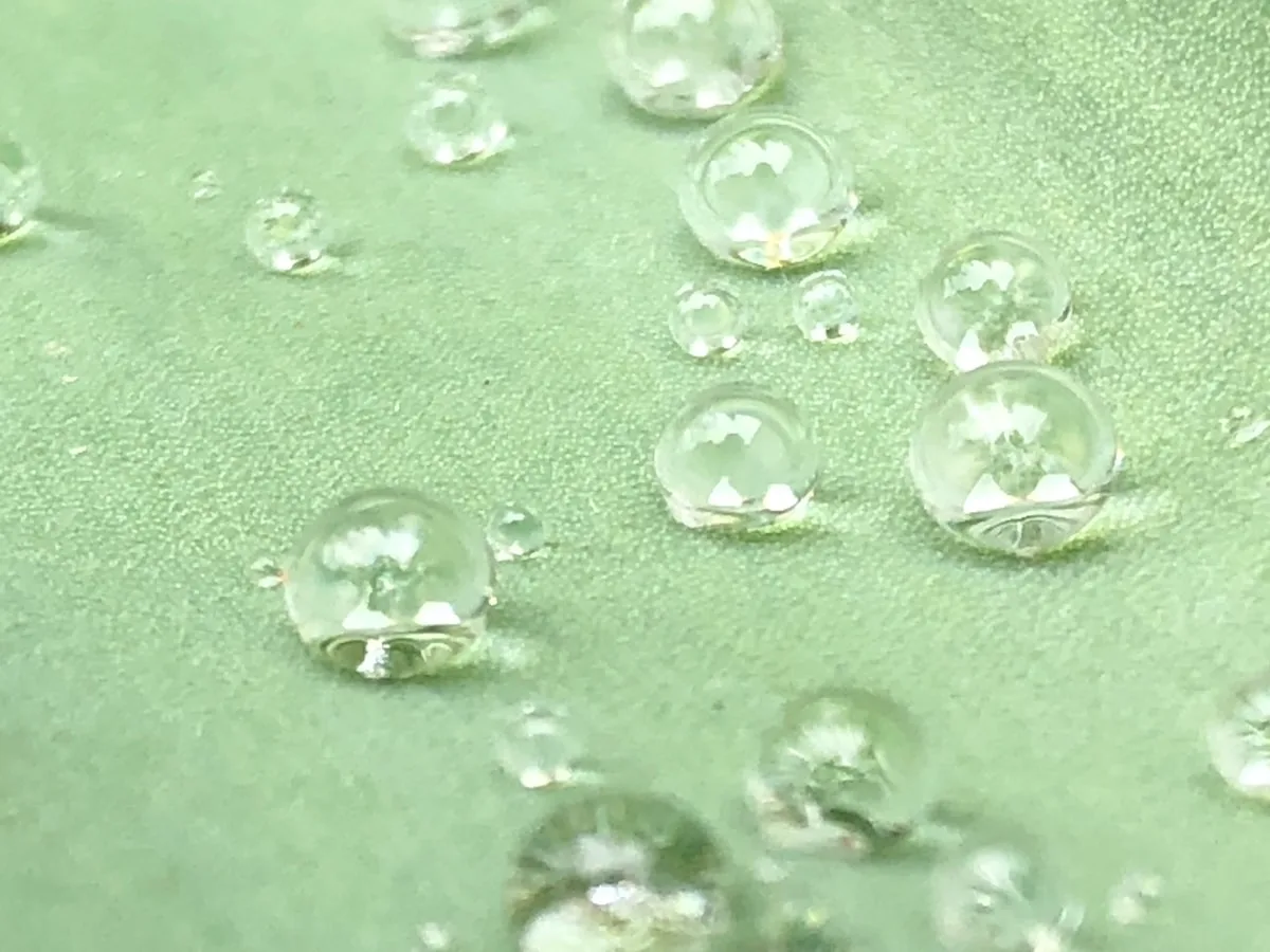 Superfície azul coberta por gotas de água condensada, ilustrando repelência em material tratado