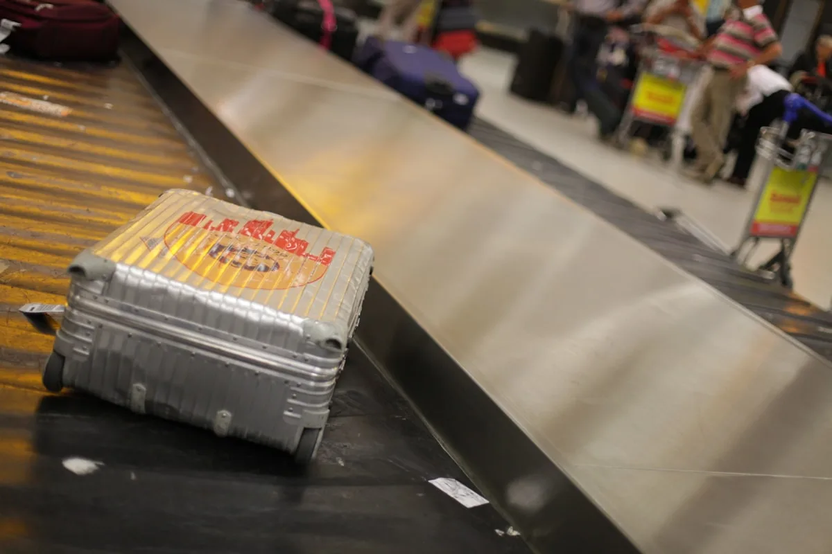 Mala rígida cinza sobre esteira de bagagem no aeroporto pronta para ser retirada após o despacho