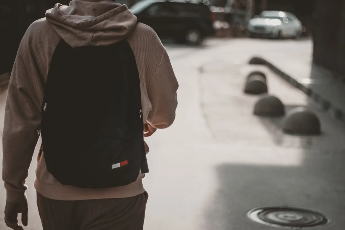 Pessoa caminhando na rua com mochila preta nas costas carregando notebook no compartimento acolchoado