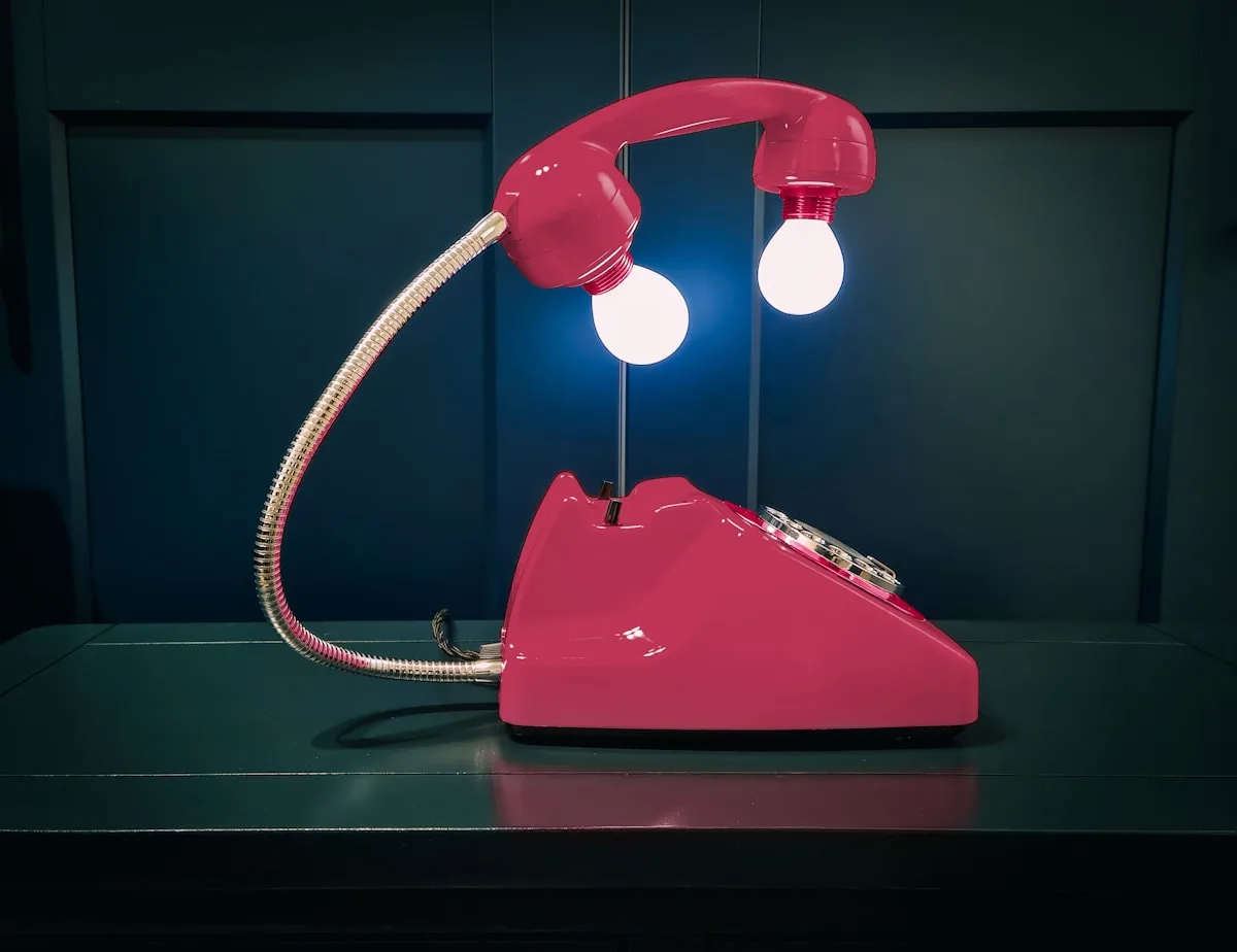 Alternativa de luz decorativa em tom quente Luminária decorativa em formato de telefone retrô com duas lâmpadas de LED brancas acesas sobre um móvel escuro