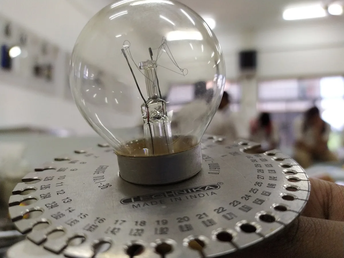 Testando a luz de uma lâmpada com equipamento de medição Lâmpada incandescente antiga presa a um disco metálico de medição com furos numerados, testada de perto