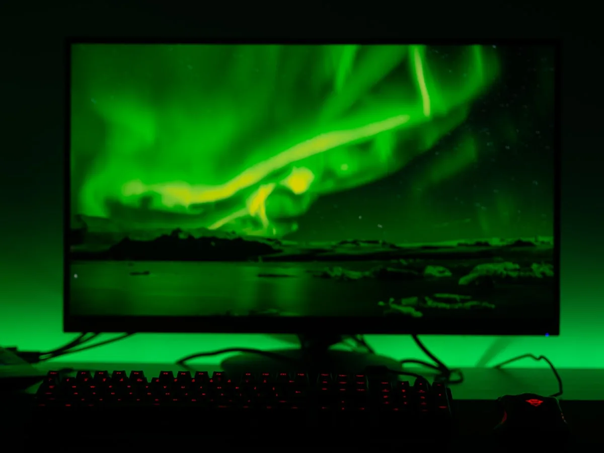 Monitor gamer com luz de fundo verde e teclado mecânico iluminado em vermelho na mesa