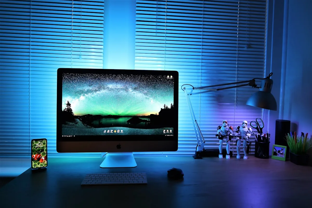 Monitor com luz ambiente azul e verde refletindo atrás da persiana