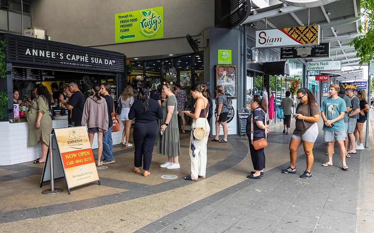 Checklist de decisão antes da pré-venda Pessoas reunidas em um corredor de mercado ao ar livre, perto de uma cafeteria, algumas conferindo o celular