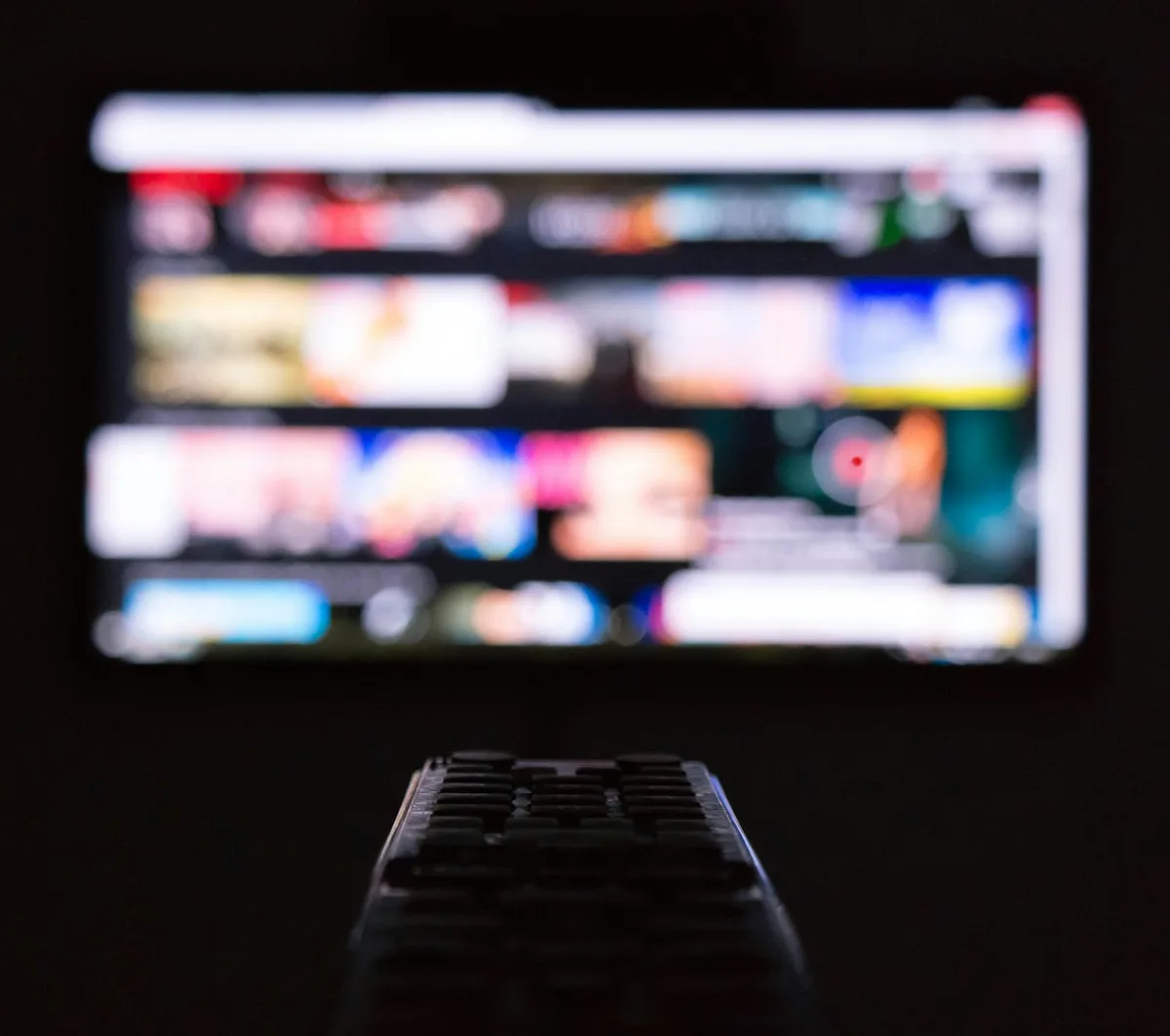 Streaming no projetor com Android TV Controle remoto em primeiro plano com uma tela de streaming desfocada ao fundo em ambiente escuro