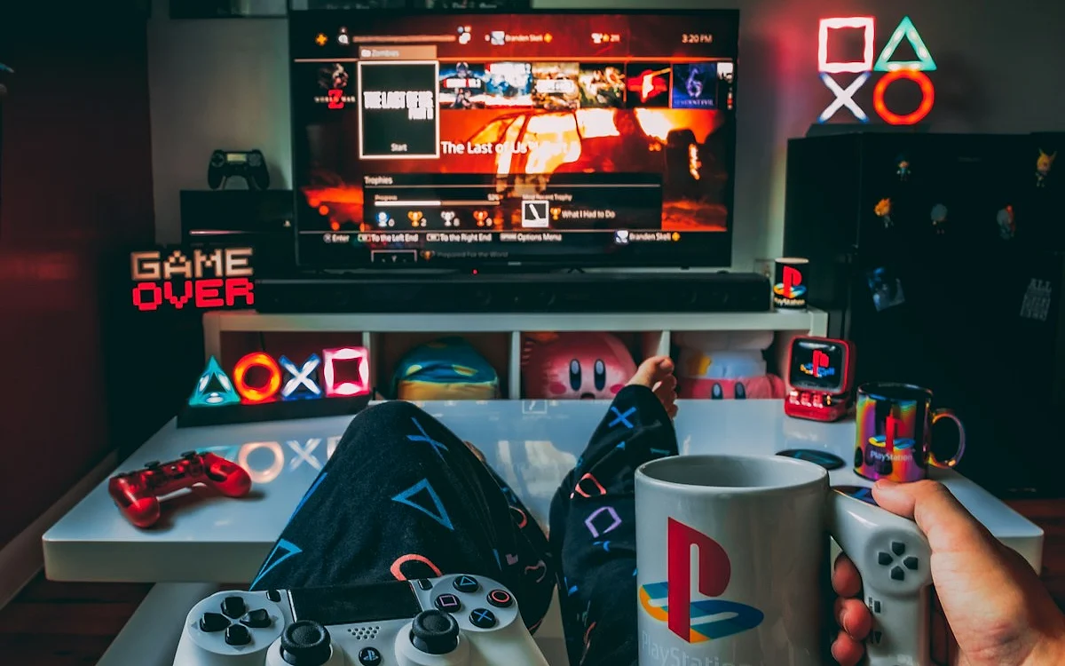 Setup de sala com TV e decoração gamer Jogador relaxando no sofá com TV exibindo menu de jogo e decoração temática PlayStation ao fundo