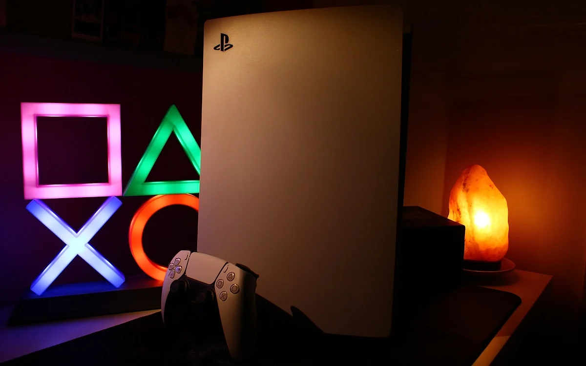 Recursos gráficos do PS5 Pro Console PlayStation 5 com o controle DualSense em ambiente decorado com luzes neon dos símbolos do PlayStation