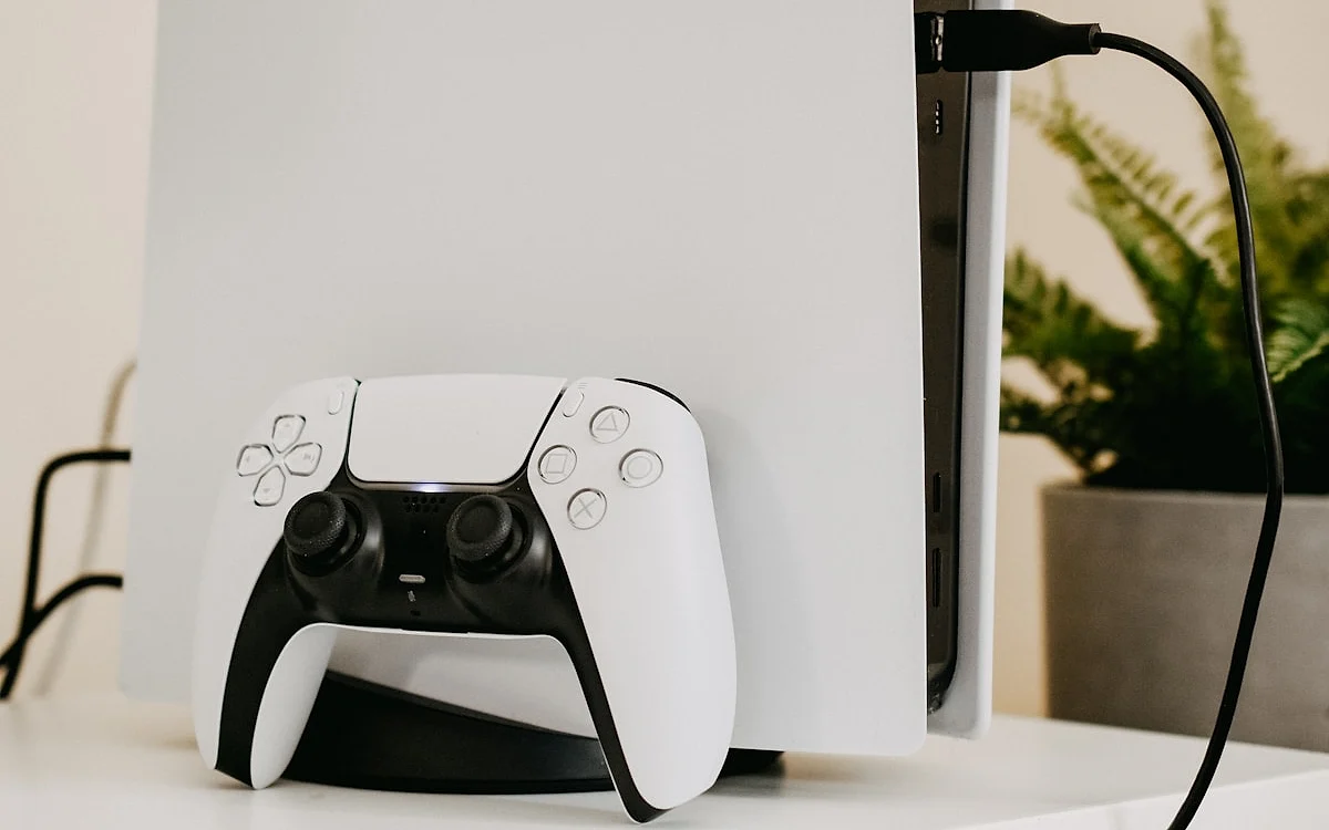 Tamanho da TV e PS5 Pro Console PlayStation 5 com o controle DualSense apoiado à frente e cabo conectado na parte de trás