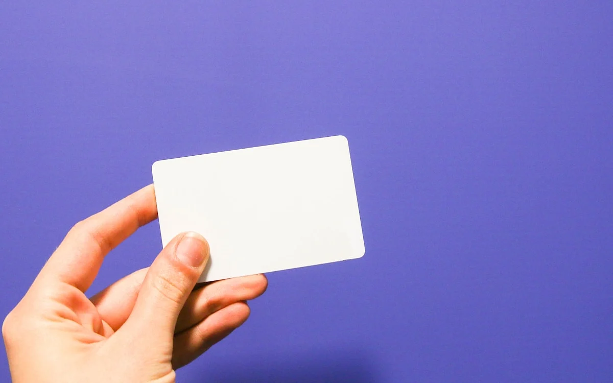 Mão segurando um cartão pré-pago branco contra fundo azul-arroxeado liso