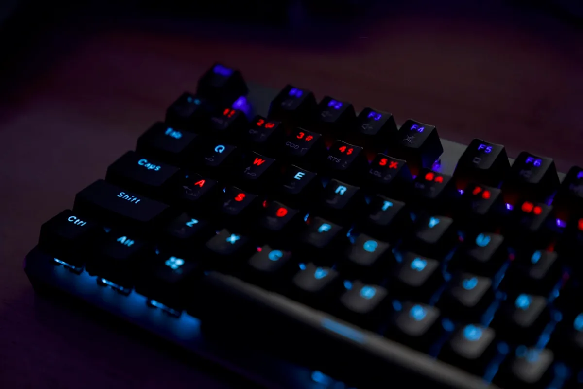 Teclado mecânico 60% compacto de bordas finas ao lado de mouse gamer em mesa escura