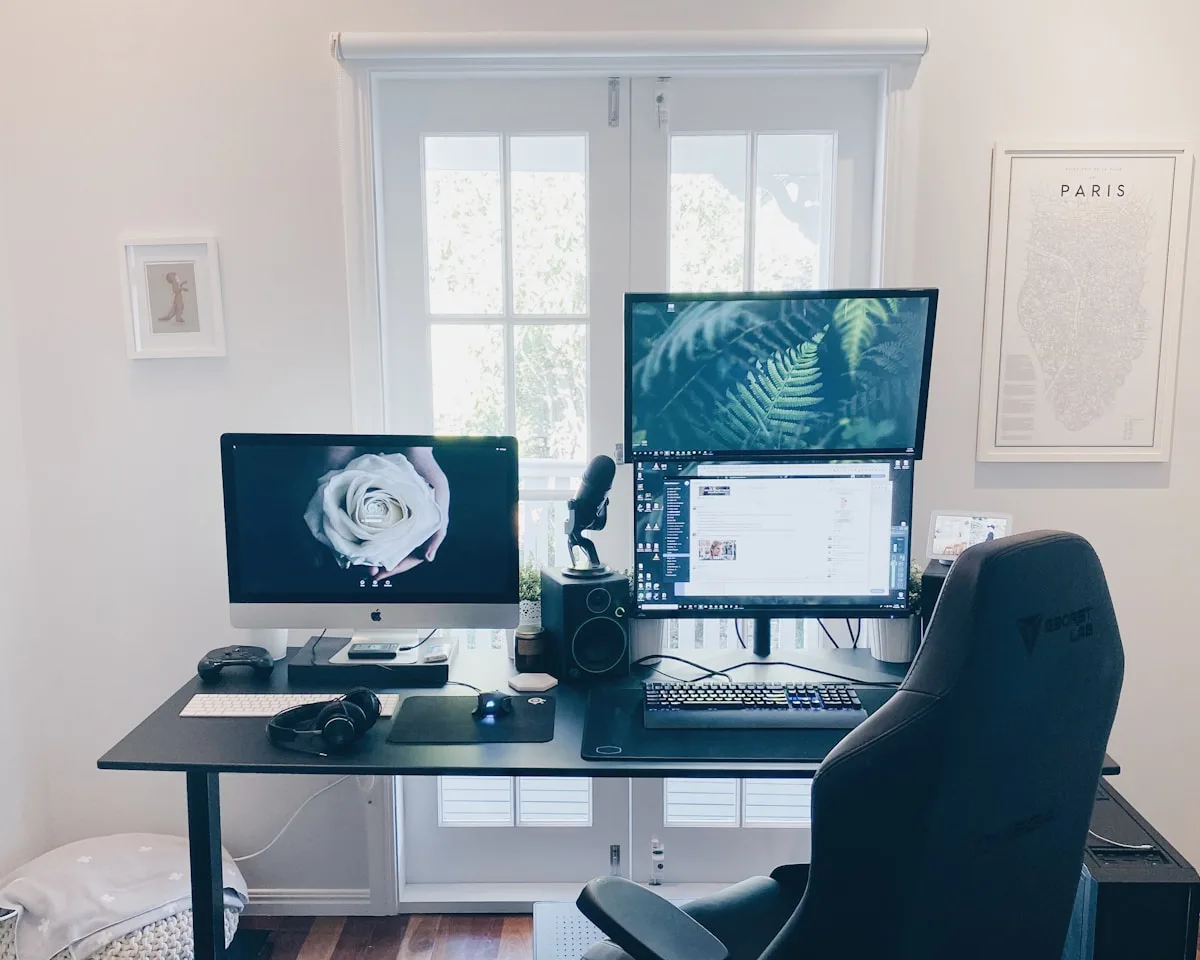 Dois monitores lado a lado em mesa de home office com braços articulados erguendo as telas