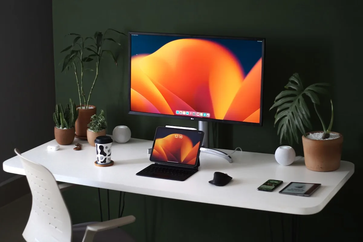 Monitor sobre braço articulado em mesa branca de home office com tablet apoiado ao lado