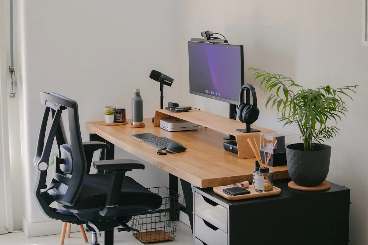 Setup com monitor sobre braço articulado e cadeira ergonômica Monitor elevado por braço articulado em mesa de madeira com cadeira ergonômica e plantas ao redor