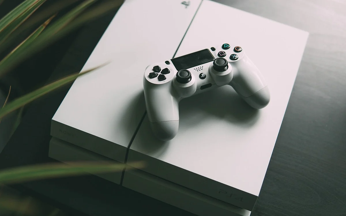 Mídia física ou digital para GTA 6 Console de videogame branco com um controle sem fio branco em cima, sobre uma mesa de madeira