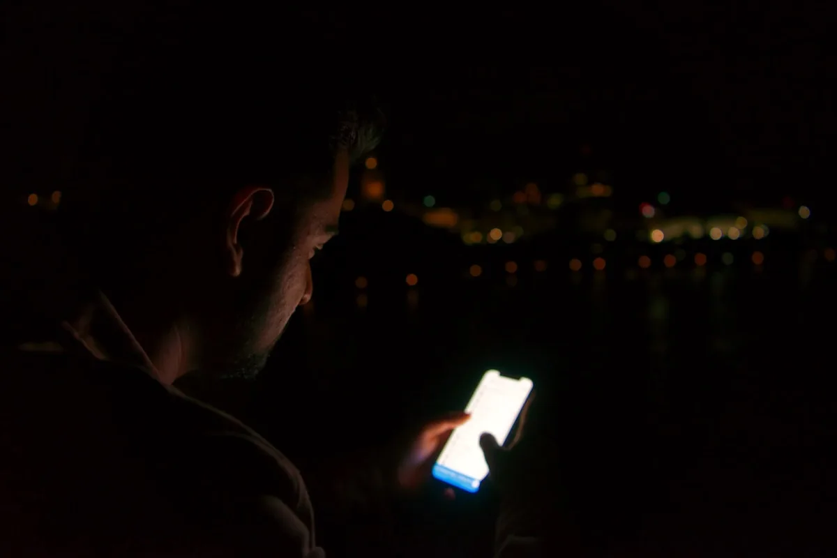 Acompanhando um vazamento em tempo real Pessoa observando a tela do celular à noite com luzes da cidade desfocadas ao fundo