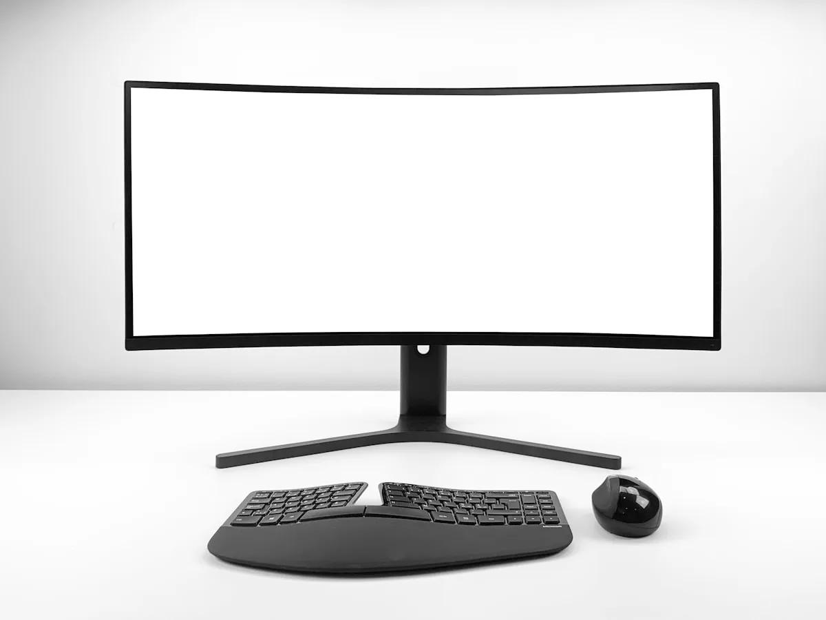 Braço de Monitor para Ultrawide Vale a Pena em 2026? Monitor ultrawide curvo apoiado no pé de fábrica ao lado de teclado ergonômico dividido e mouse