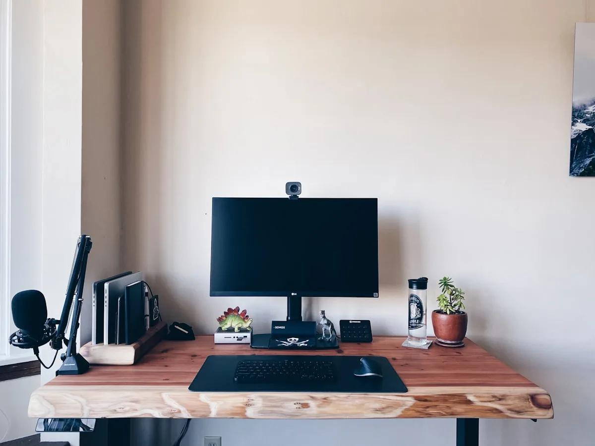 Como Instalar Suporte de Monitor Articulado: Passo a Passo Monitor preso a braço articulado fixado na borda de uma mesa de madeira com microfone ao lado