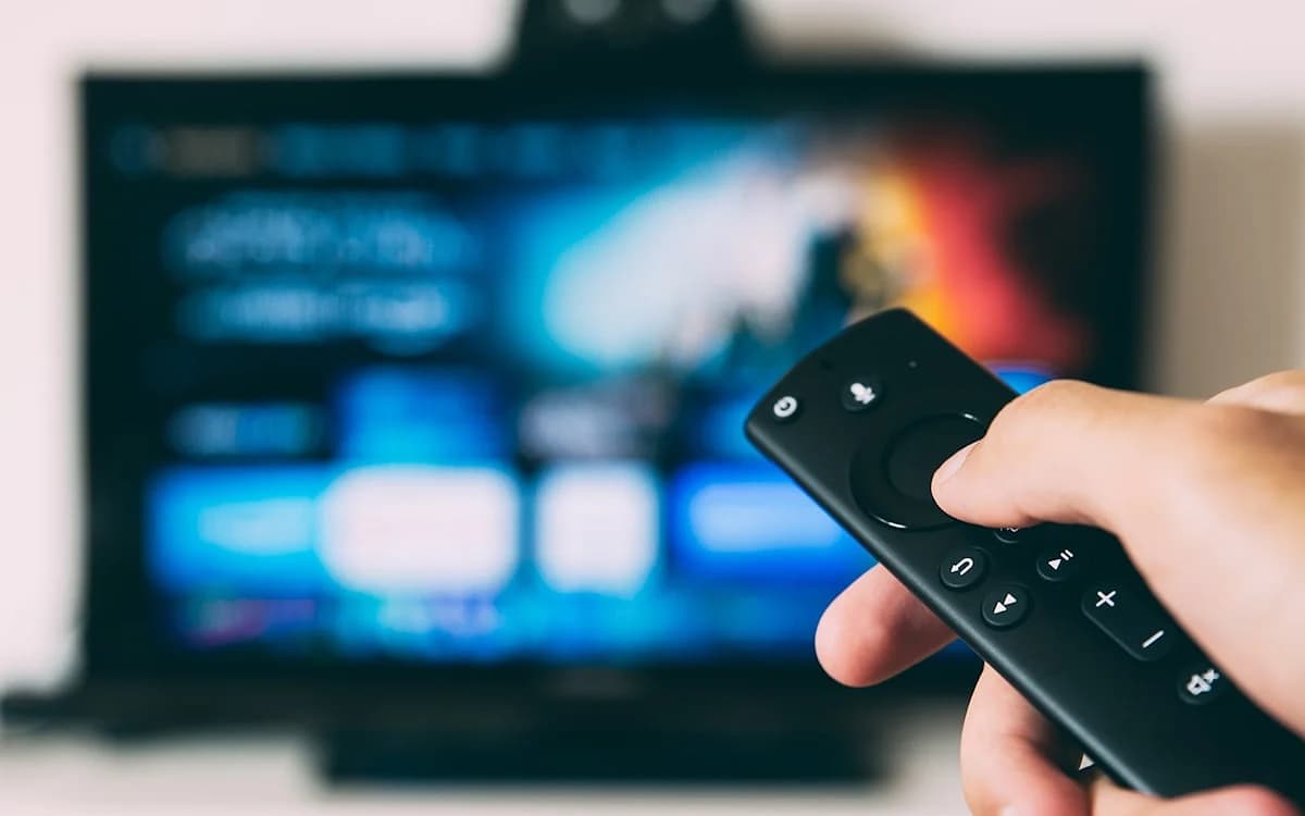 Streaming por assinatura na TV Controle remoto apontado para uma TV com menu desfocado de aplicativos de streaming