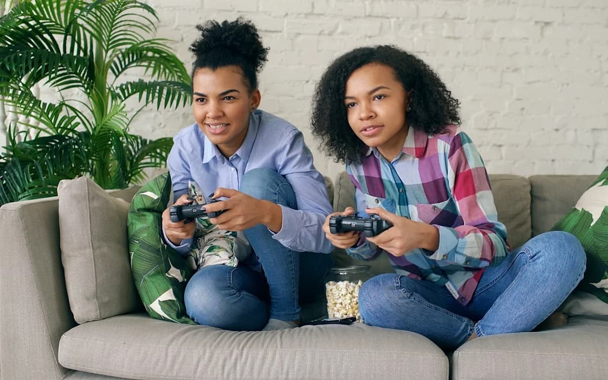 GTA Online 2: o que já se sabe Duas jogadoras sentadas no sofá seguram controles enquanto jogam juntas em modo multiplayer