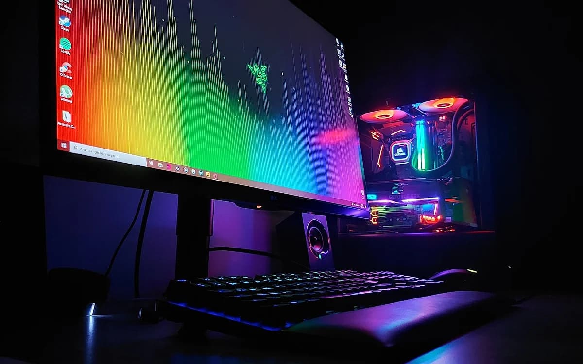 Melhor Mini PC Gamer 2026: Ranking e Guia de Compra Monitor com papel de parede colorido ao lado de gabinete RGB aceso, teclado e caixa de som em primeiro plano