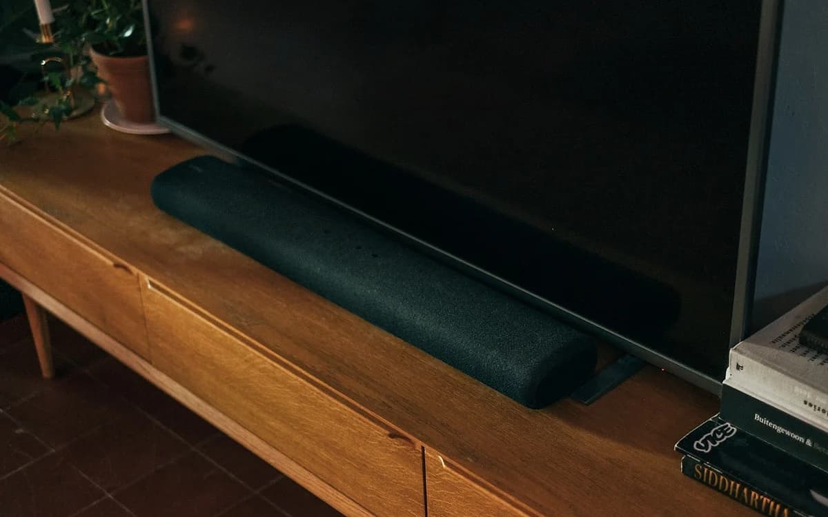 Melhor Soundbar para TV Custo-Benefício 2026 Soundbar posicionada abaixo de uma TV na sala com subwoofer sem fio ao lado