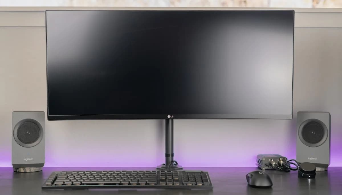 Melhor Suporte de Monitor Articulado em 2026 Monitor ultrawide LG apoiado em suporte articulado com pistão a gás sobre mesa preta
