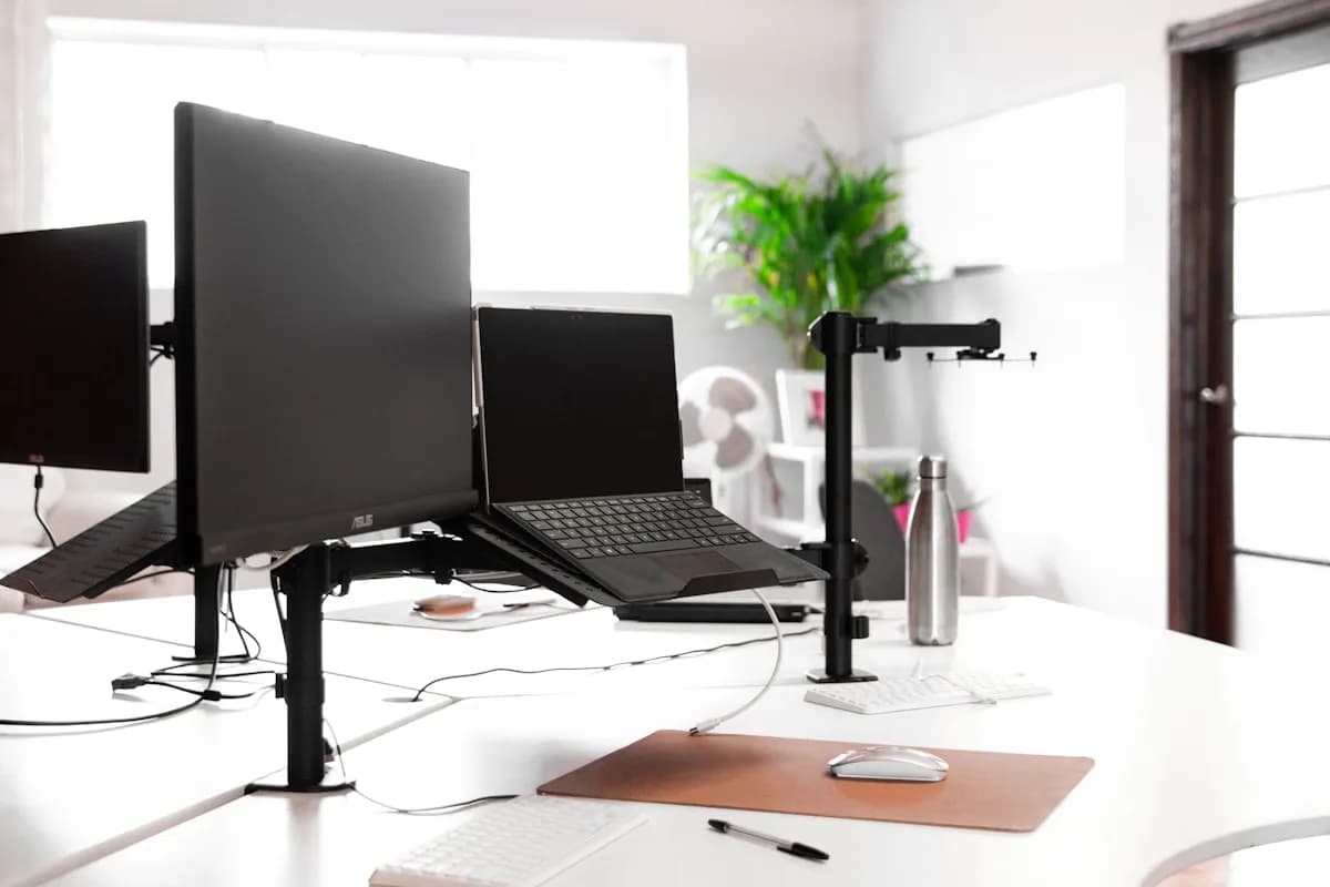Melhor Suporte para Notebook e Monitor em 2026 Notebook elevado em bandeja articulada ao lado de monitor externo sobre suporte de mesa