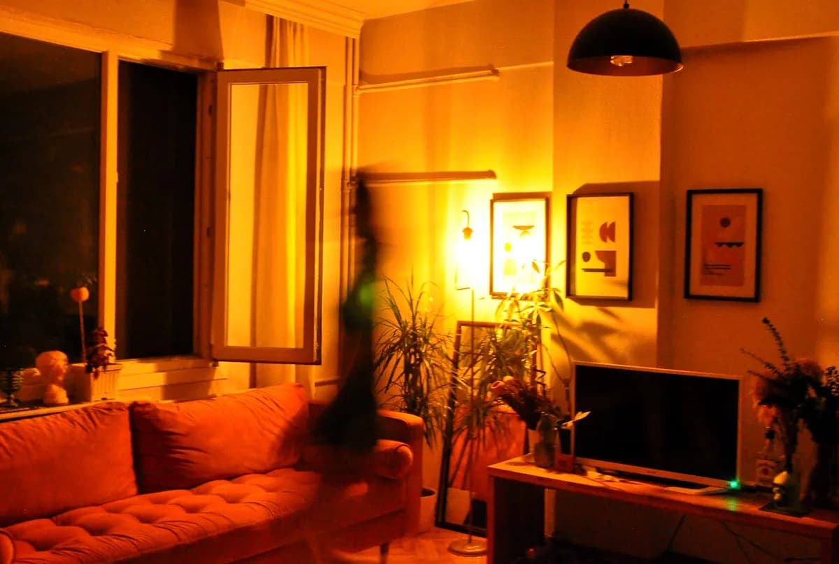 O Que É Bias Lighting e Para Que Serve Sala escura à noite iluminada por luz âmbar suave ao redor de estante e tela pequena
