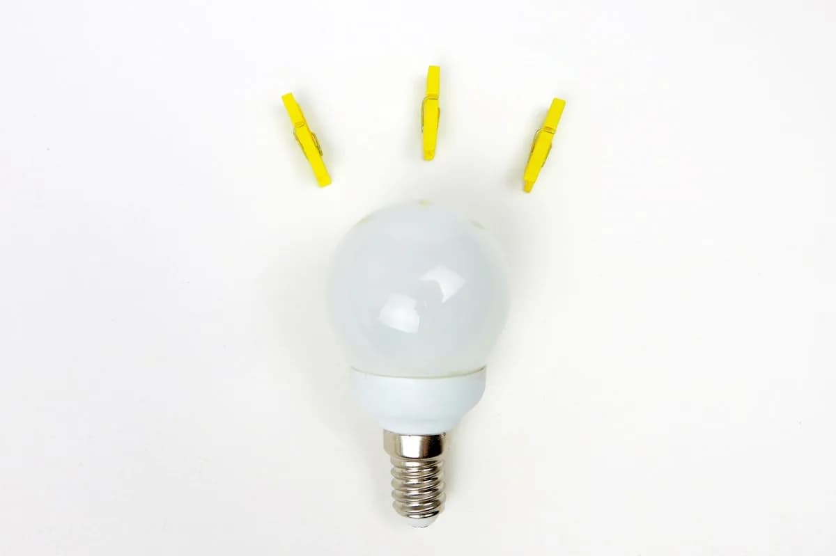 O Que É Lúmens ANSI e Por Que o Número da Caixa Mente Lâmpada LED redonda vista de cima, com três prendedores amarelos formando raios de luz ao redor
