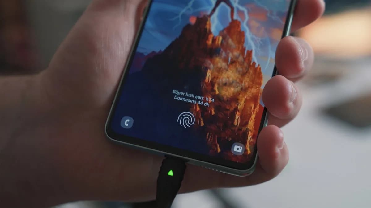 Bateria do Steam Deck: Quanto Dura de Verdade em 2026 Mão segurando um aparelho conectado a um cabo de carregamento com porcentagem de bateria na tela