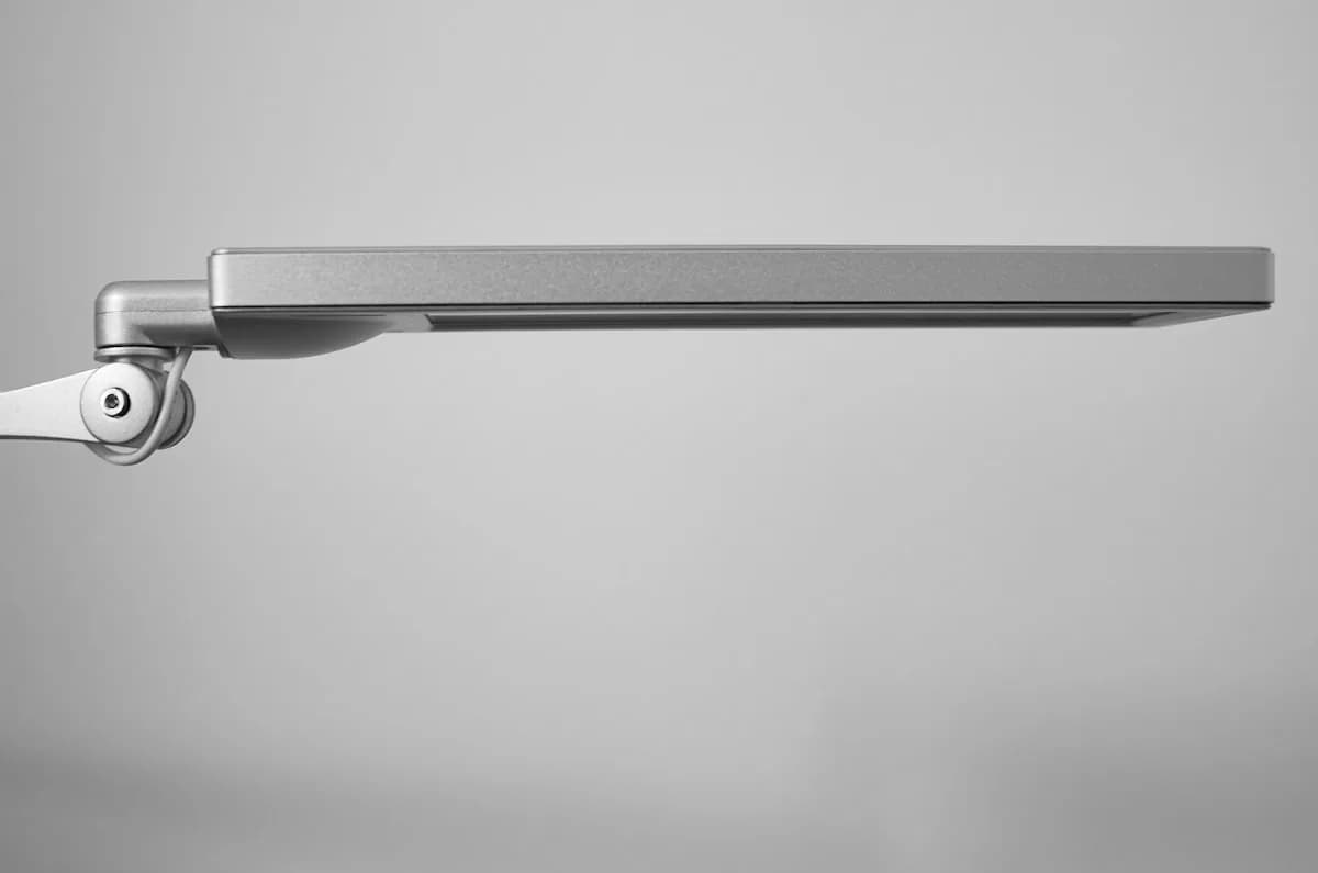 Quanto Peso um Suporte de Monitor Aguenta Perfil lateral de um braço articulado de metal com a junta do pistão visível sobre fundo neutro
