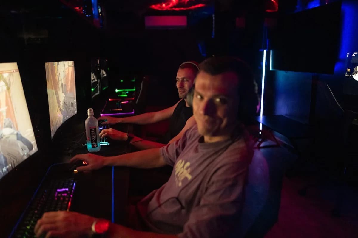 ROG Ally Vale a Pena em 2026? Prós e Contras Jogadores concentrados em estações de PC dentro de um espaço de LAN house com luzes neon