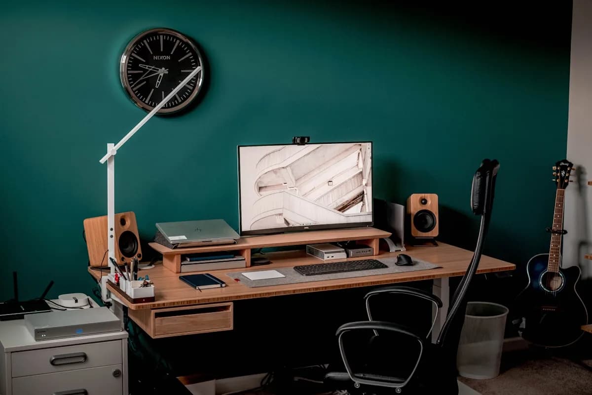 Suporte de Monitor ou Braço de Microfone: Qual a Diferença Monitor sobre mesa de madeira em home office com braço articulado de luminária e teclado ao lado