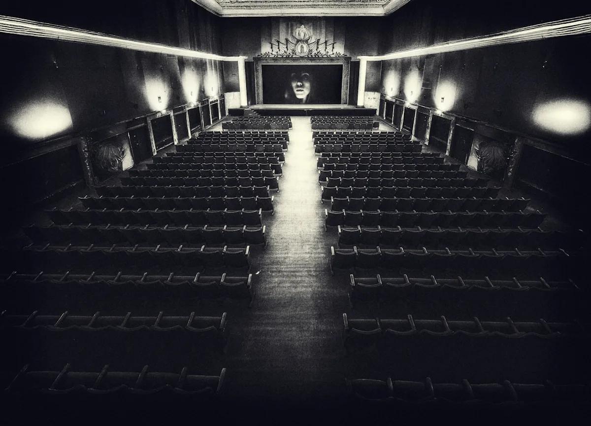 Tela de Projeção Vale a Pena em 2026 Interior de cinema antigo em preto e branco, fileiras de poltronas vazias voltadas para a tela grande