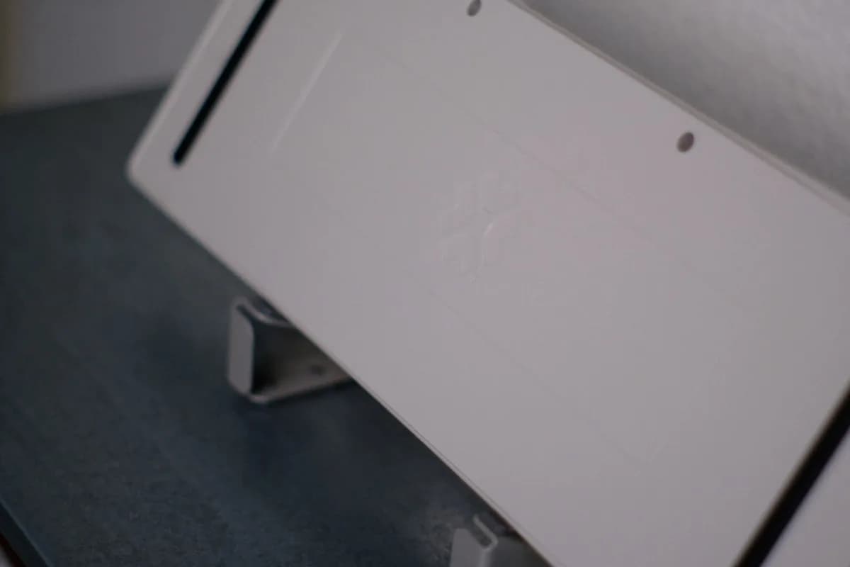 VESA 75 ou 100: Qual a Diferença Entre os Padrões Placa de adaptação branca presa por um suporte com grampo sobre uma mesa escura