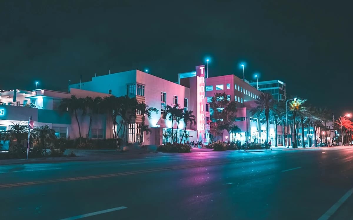 Vice City em GTA 6: o cenário que inspira a cidade Prédios art déco iluminados por neon rosa e azul em avenida litorânea com palmeiras à noite