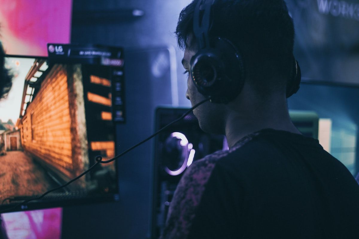Homem jogando CS2 com headset e monitor Homem usando headset enquanto joga CS2, focado na tela do computador