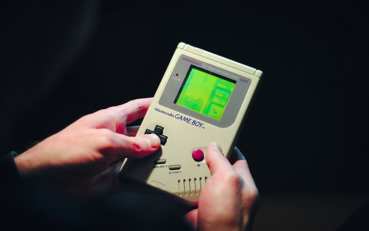 Game Boy cinza em mãos: nostalgia e jogos clássicos Pessoa segurando um Game Boy cinza, simbolizando nostalgia dos jogos clássicos