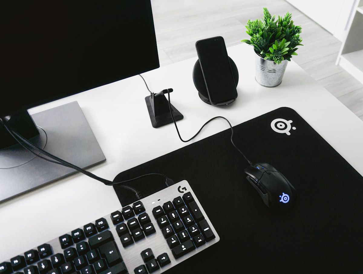 Teclado gamer magnético em greyscale ao lado de mouse Teclado magnético gamer em preto e branco ao lado de um mouse sobre a mesa