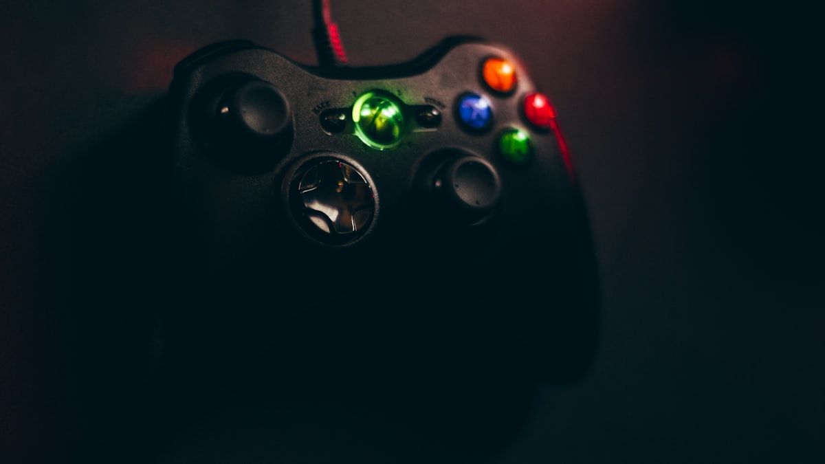 Controle Xbox 360 Preto Ideal para Jogos Riot Games Controle com fio Xbox 360 preto sobre superfície preta, ideal para jogos da Riot Games.
