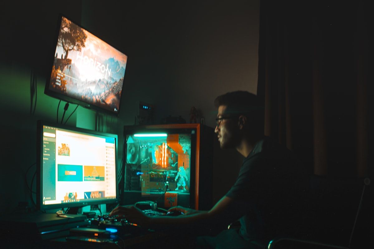 Homem em camisa preta usando computador gamer para jogar Homem de camisa preta sentado em frente ao computador gamer, focado em sua experiência de jogo