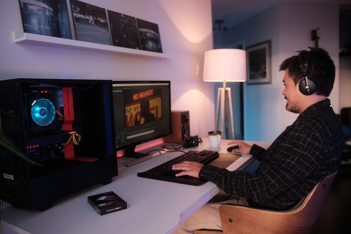 Homem concentrado em computador gamer com fones de ouvido Homem usando fones de ouvido enquanto trabalha em um computador gamer na mesa